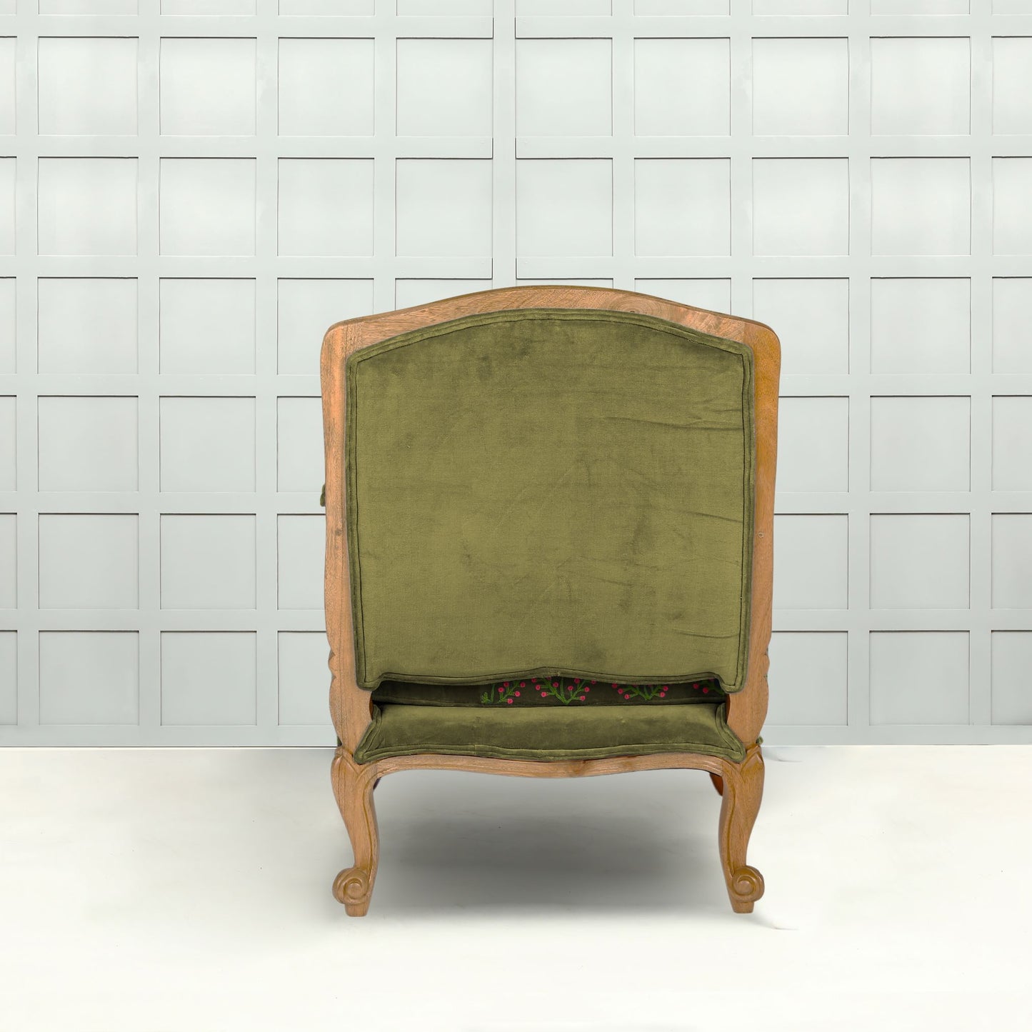 Back view of A grass green velvet upholstered armchair with a floral embroidered design and carved wooden frame, displayed against a white tiled background.
