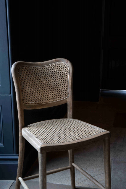Close up of A barstool with a natural rattan and a wood finish. The stool has a rattan backrest and is placed against a dark background.