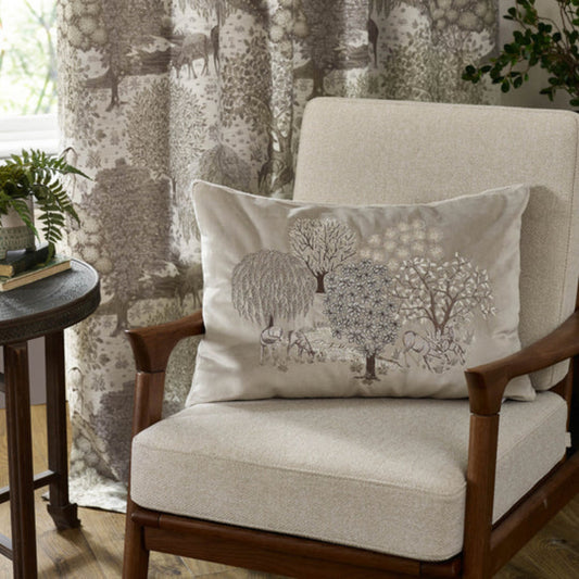 Chair with a decorative pillow featuring trees and animals in a room with curtains and a side table.