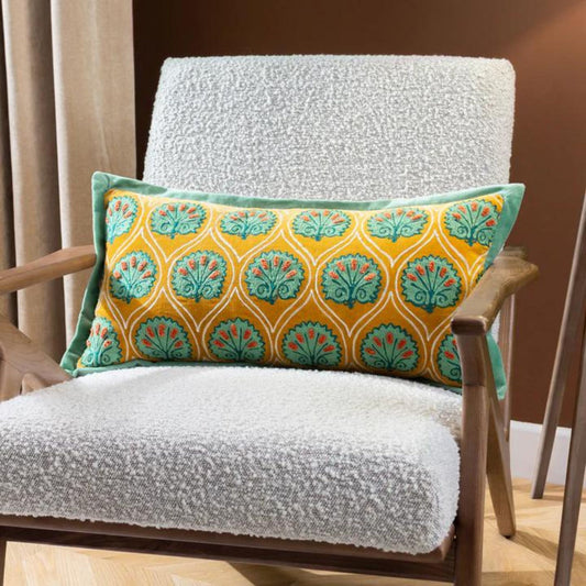 A rectangular mustard and green embroidered cushion with a floral pattern, placed on a white sofa cushion on a wooden chair.