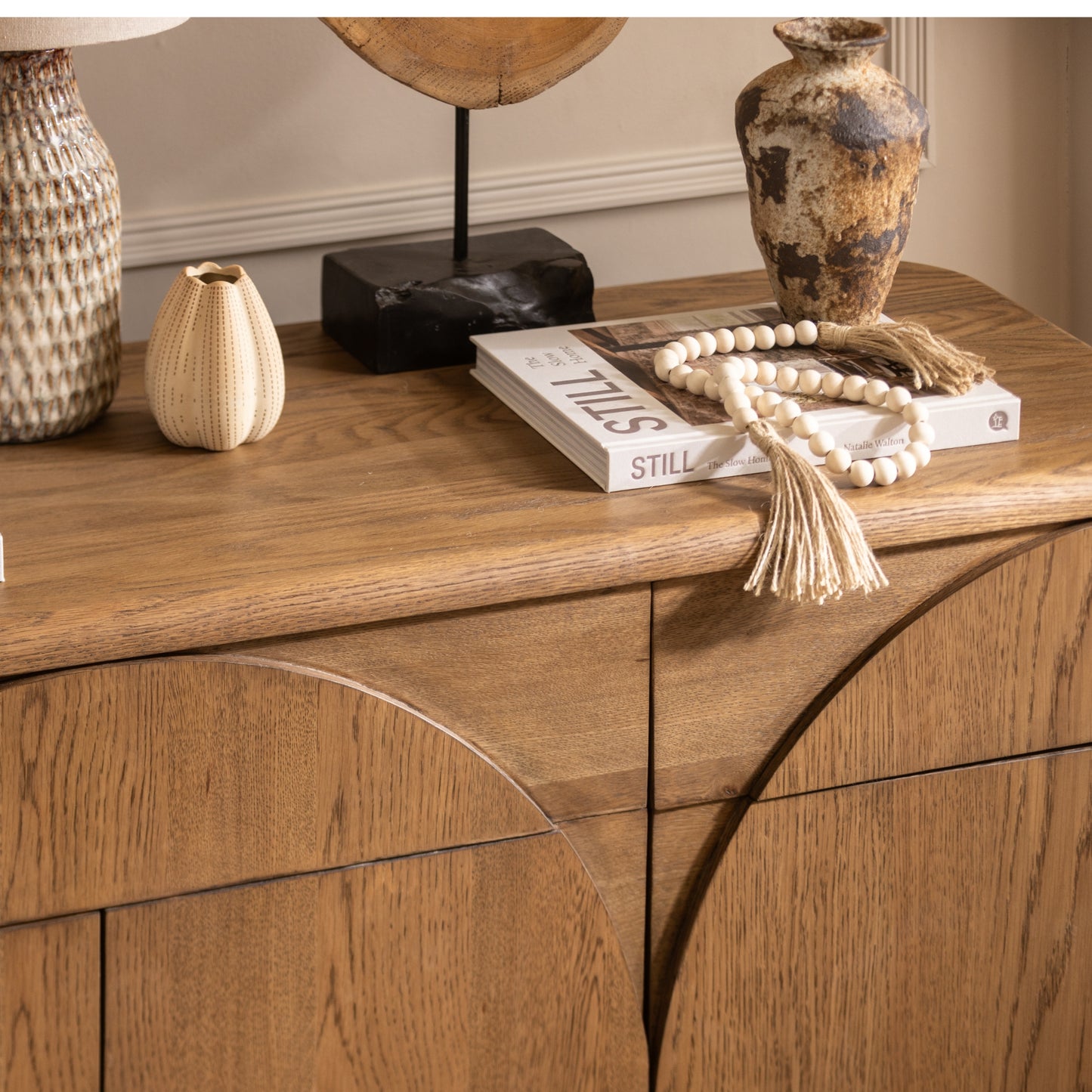 Wooden sideboard with decorative items including a vase, book, and beads.