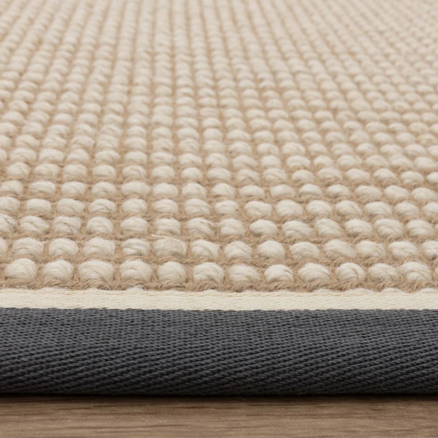 Close-up of a textured beige rug with a black border on a wooden floor.