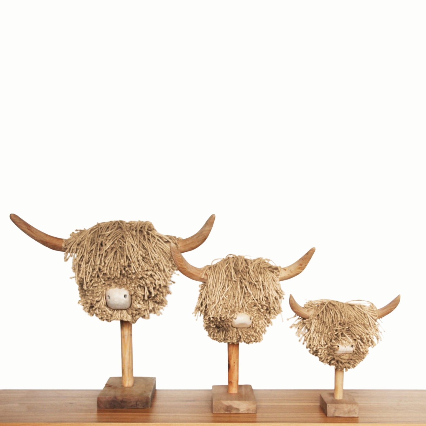 Three decorative heads of highland cows made from jute on wooden stands against a white background.