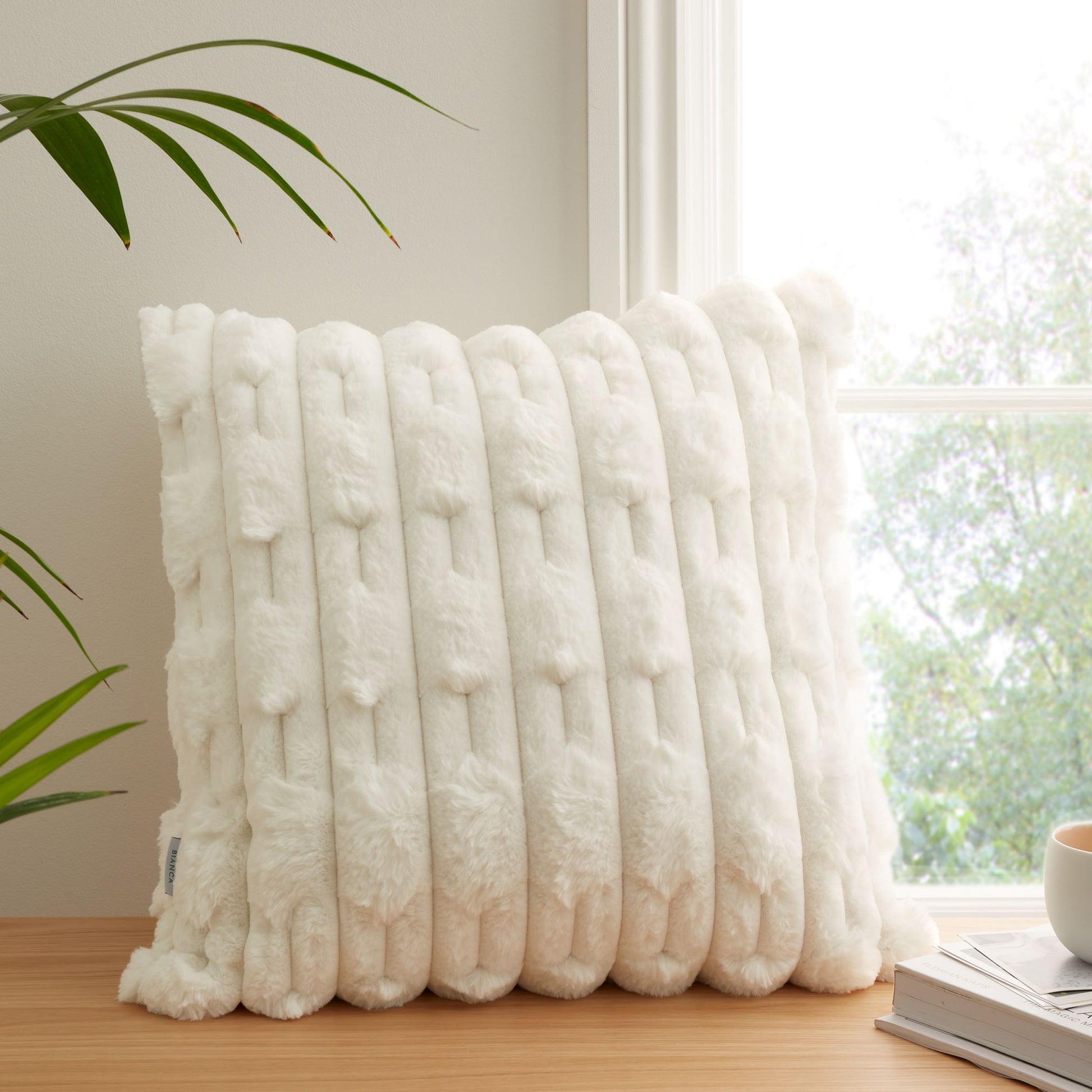Faux Fur cream cushion sitting on a wooden shelf next to a window