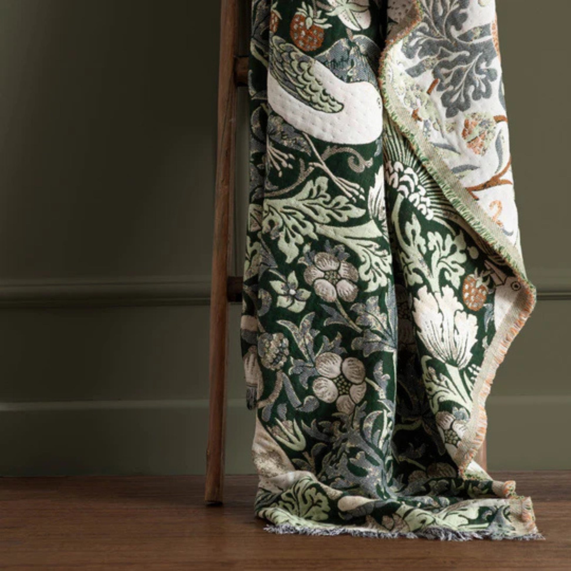 Floral patterned blanket draped over a wooden ladder against a neutral wall.