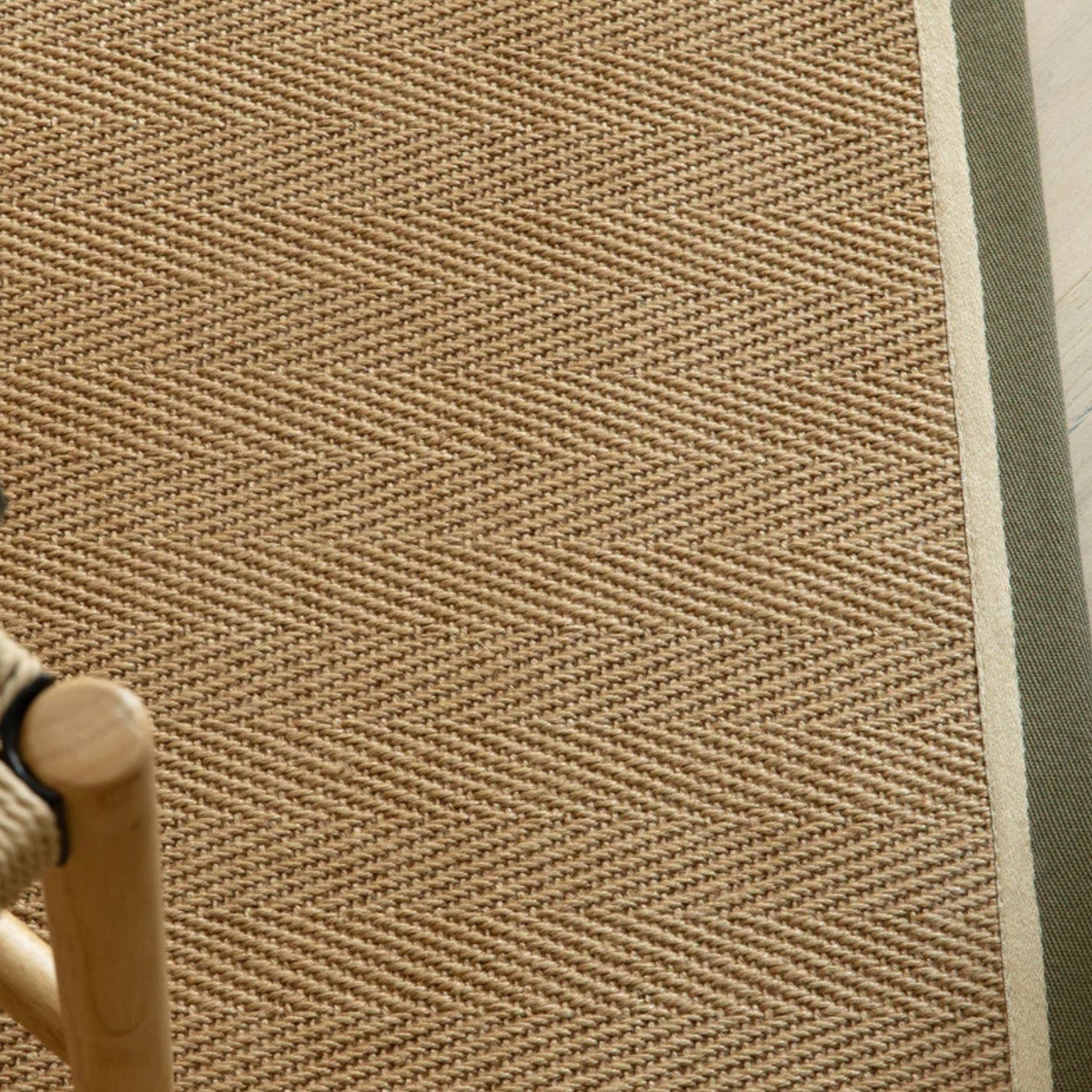 Close-up of a textured beige rug with a chair leg partially visible.
