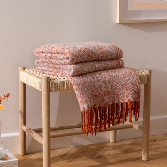 Folded Herringbone rust throw blanket on a wooden stool with a neutral background