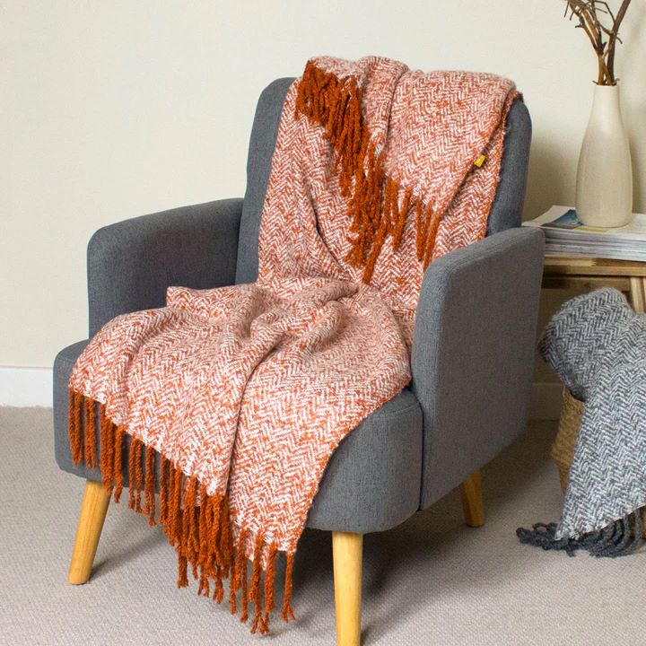 Herringbone fringed rust throw draped over a grey armchair