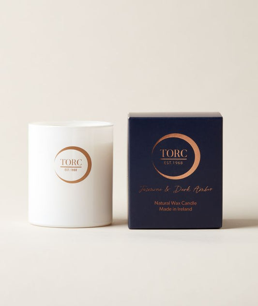 White candle with gold logo next to a blue box with gold text on a beige background