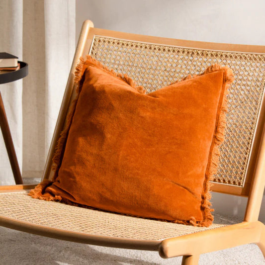 Orange fringed cushion on a ratton chair