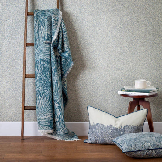 Indigo patterned blanket draped over a wooden ladder against a textured wall with decorative pillows on the floor.