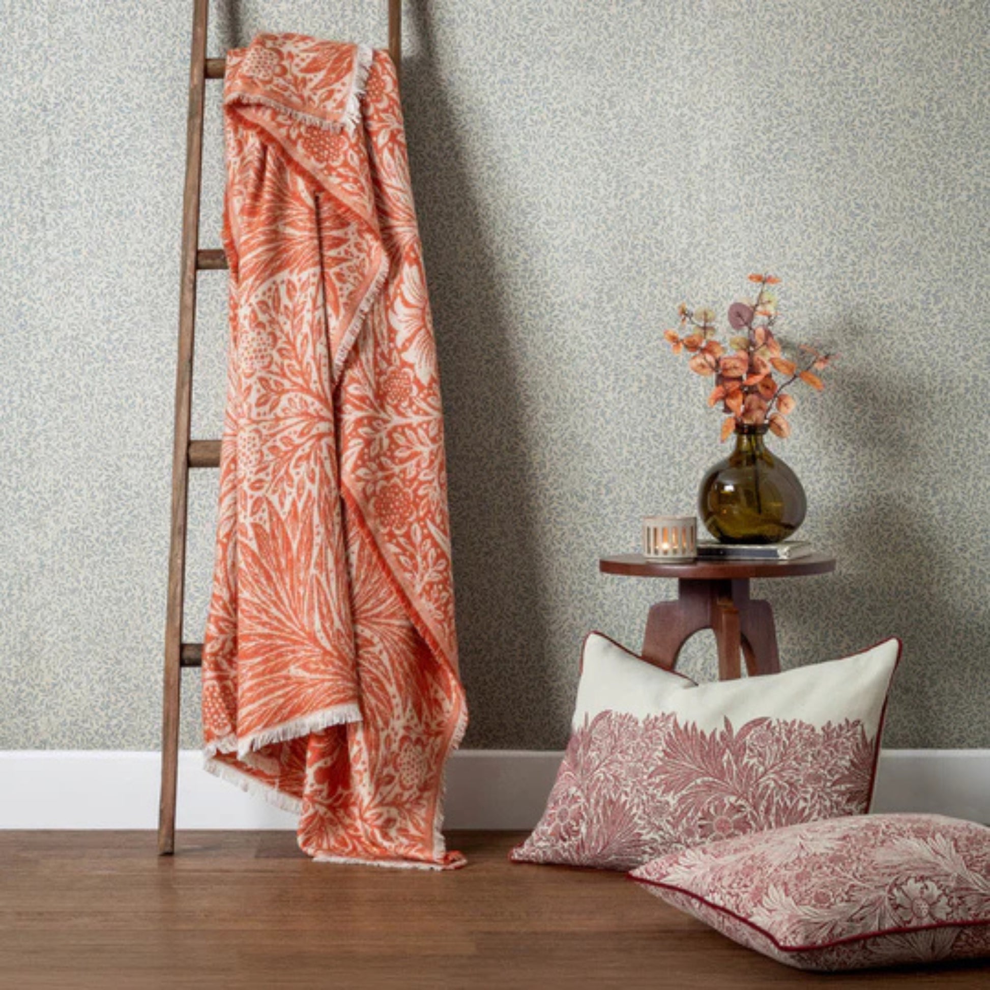 Patterned blanket draped over a wooden ladder against a textured wall with a small table and decorative items.