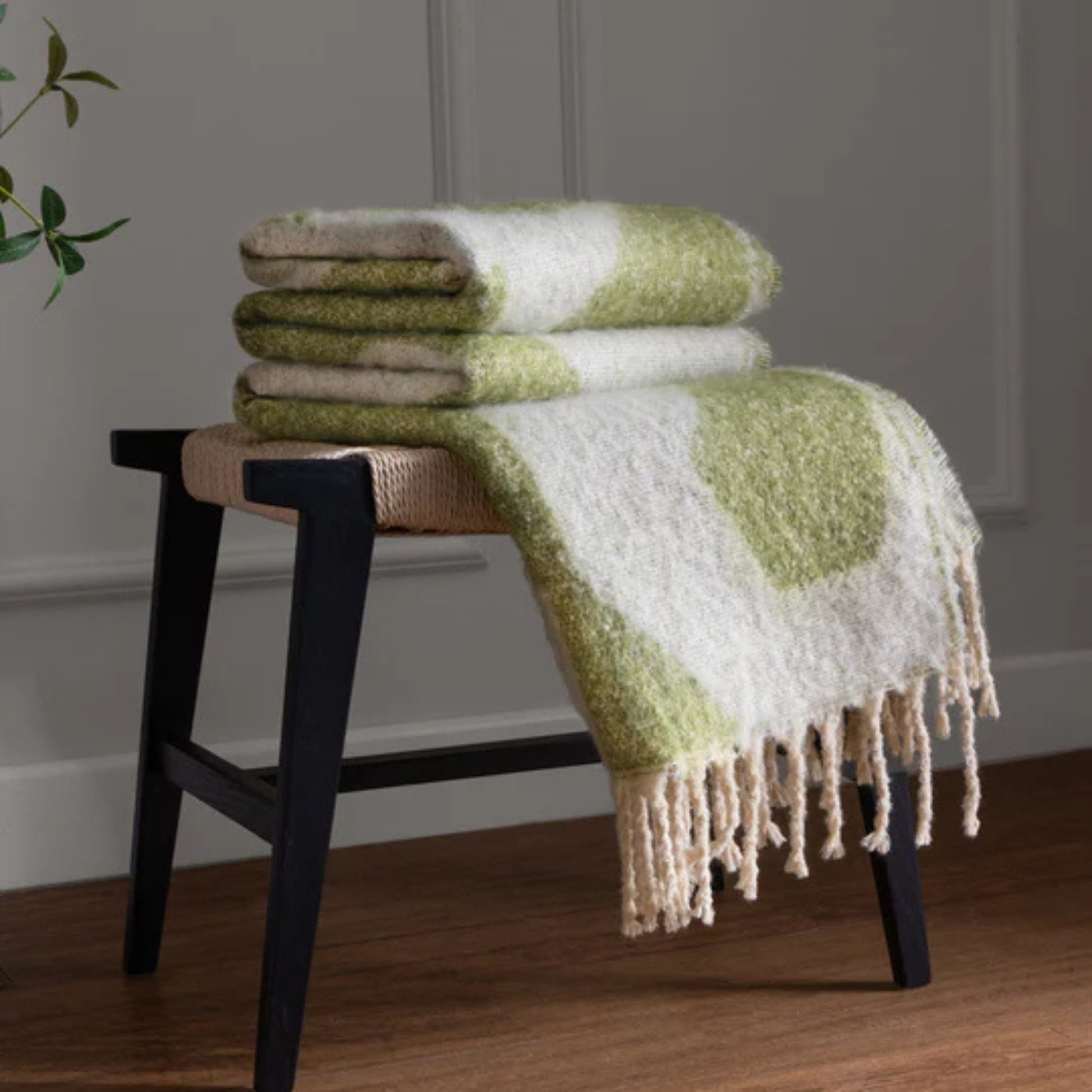 Green and white patterned blanket draped over a wooden stool against a gray wall.