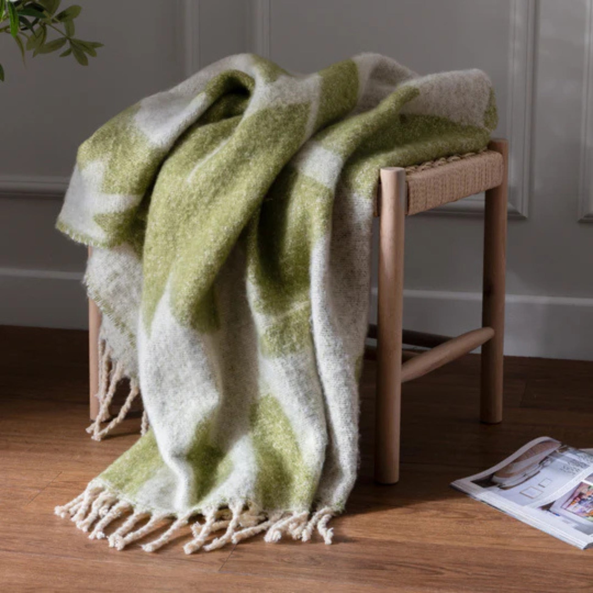 Green and white patterned blanket draped over a wooden stool on a wooden floor.