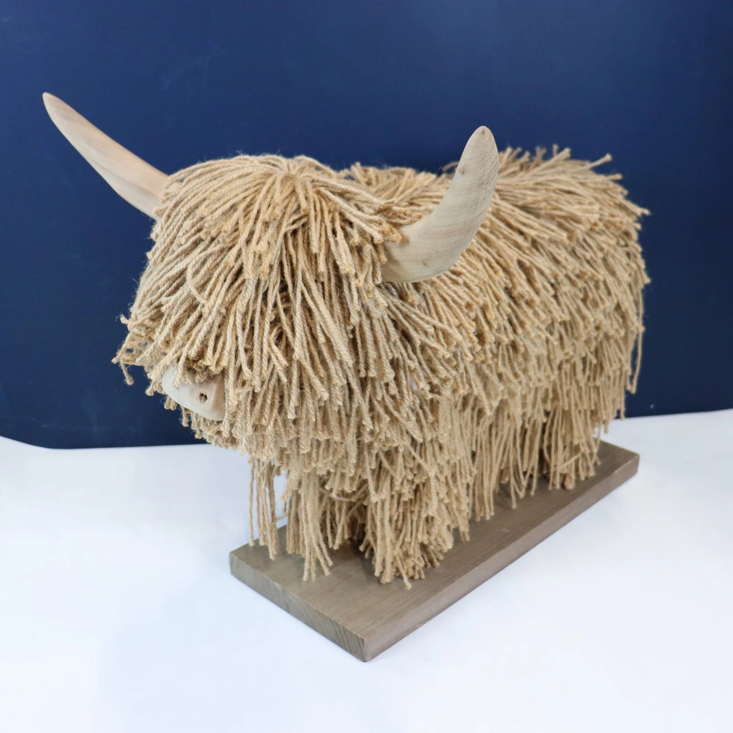 Model of a highland cow made from jute and wood on a white surface with a blue background