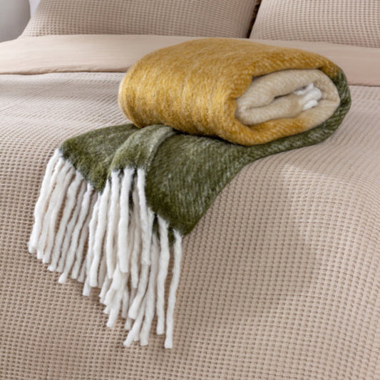 Green and yellow blanket with fringes on a beige sofa