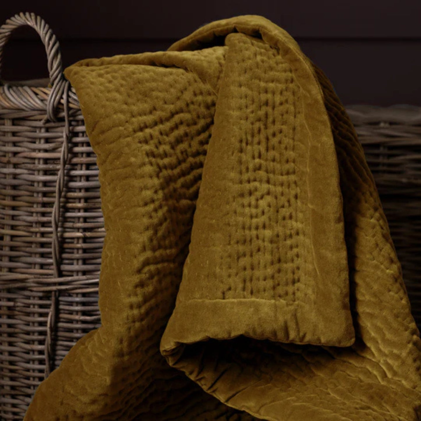 Mustard textured velvet blanket draped over a wicker basket on a dark background