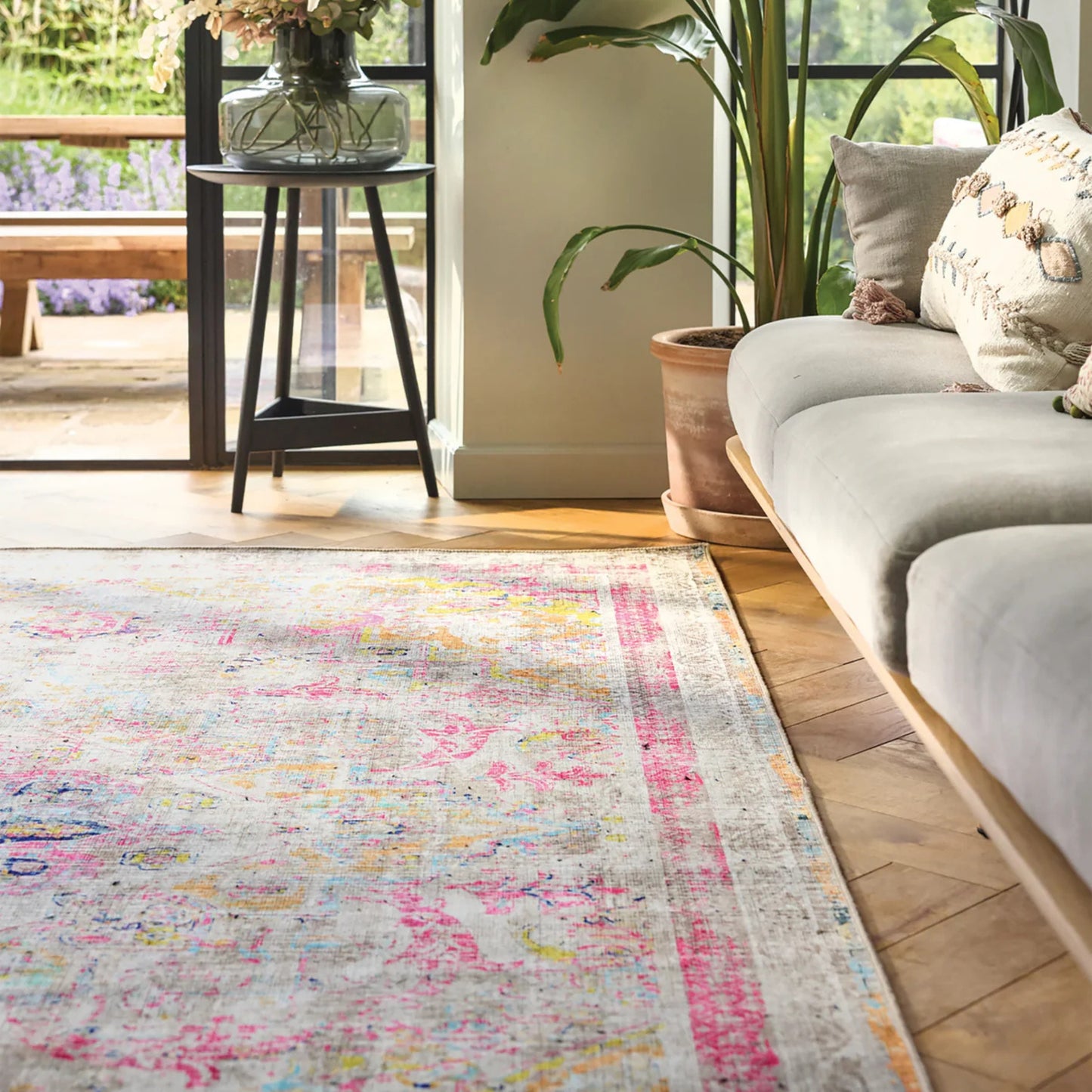 Living room with a colorful rug, gray sofa, and plants.