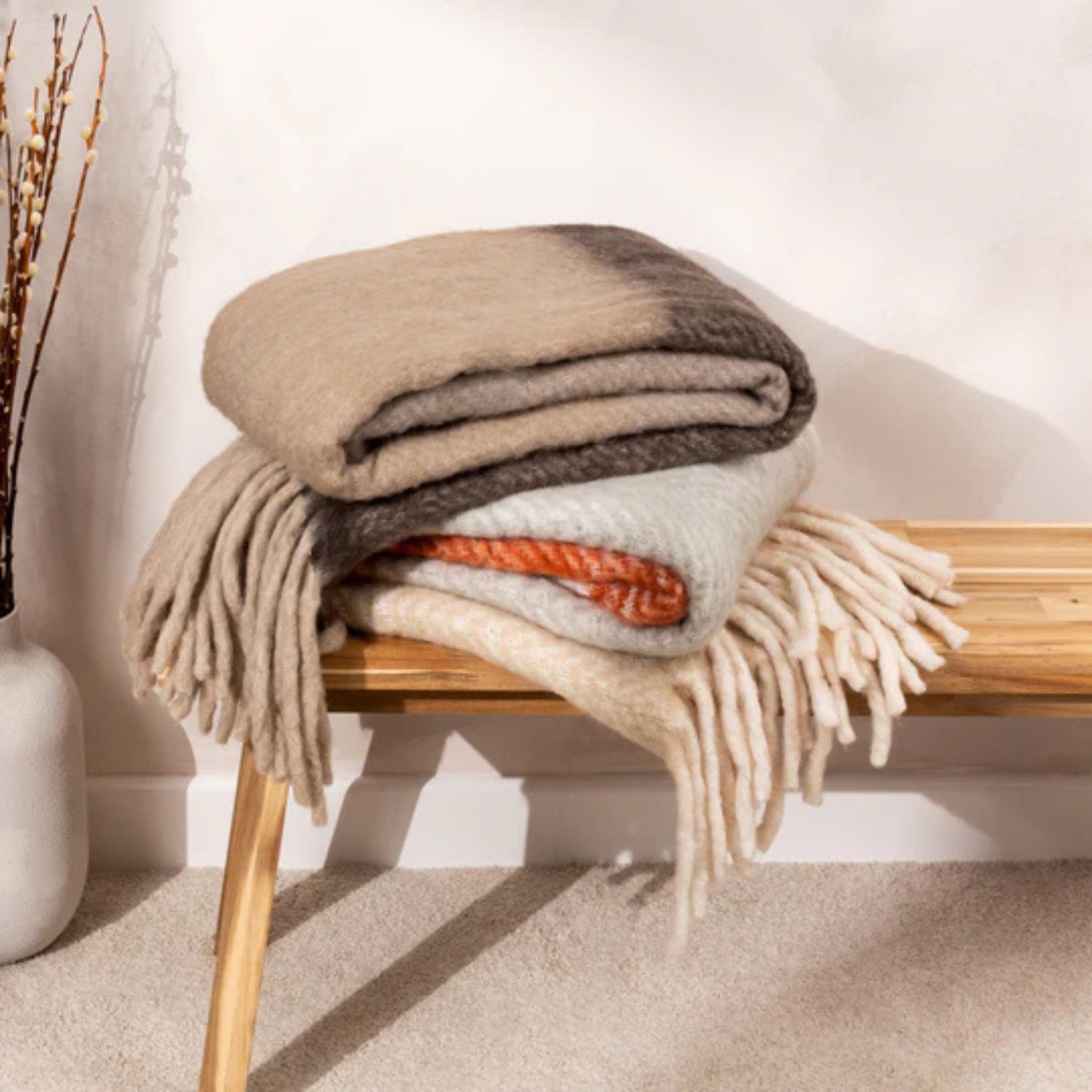 Stack of folded blankets on a wooden stool with a neutral background