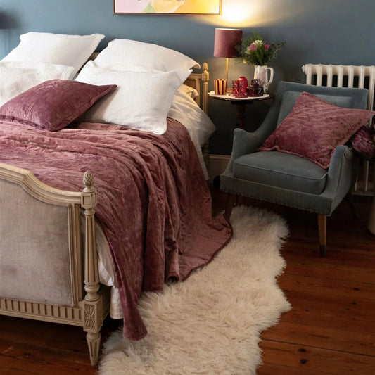 Bedroom setting with double bed dressed in white linen and velvet pink bedspread with blue accent chair at side with small side table and lamp