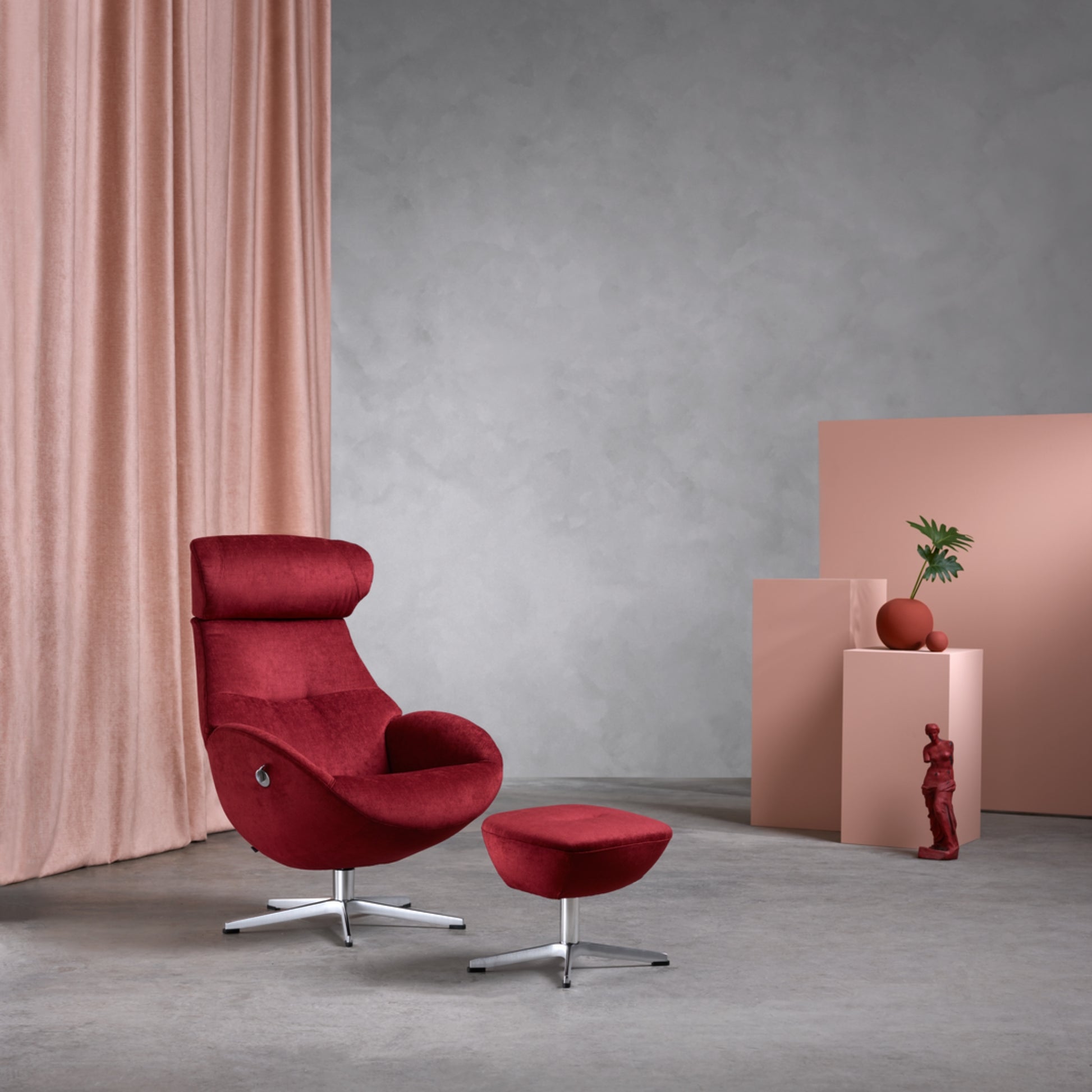Red armchair and foot stool with a grey wall and pink curtain in the background