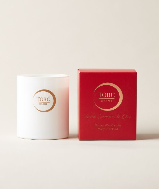 A white tumbler candle with the brand Torc next to a red box with the same Torc logo in gold