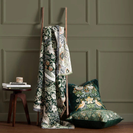 Decorative green fabric with floral patterns draped over a wooden ladder against a green paneled wall.