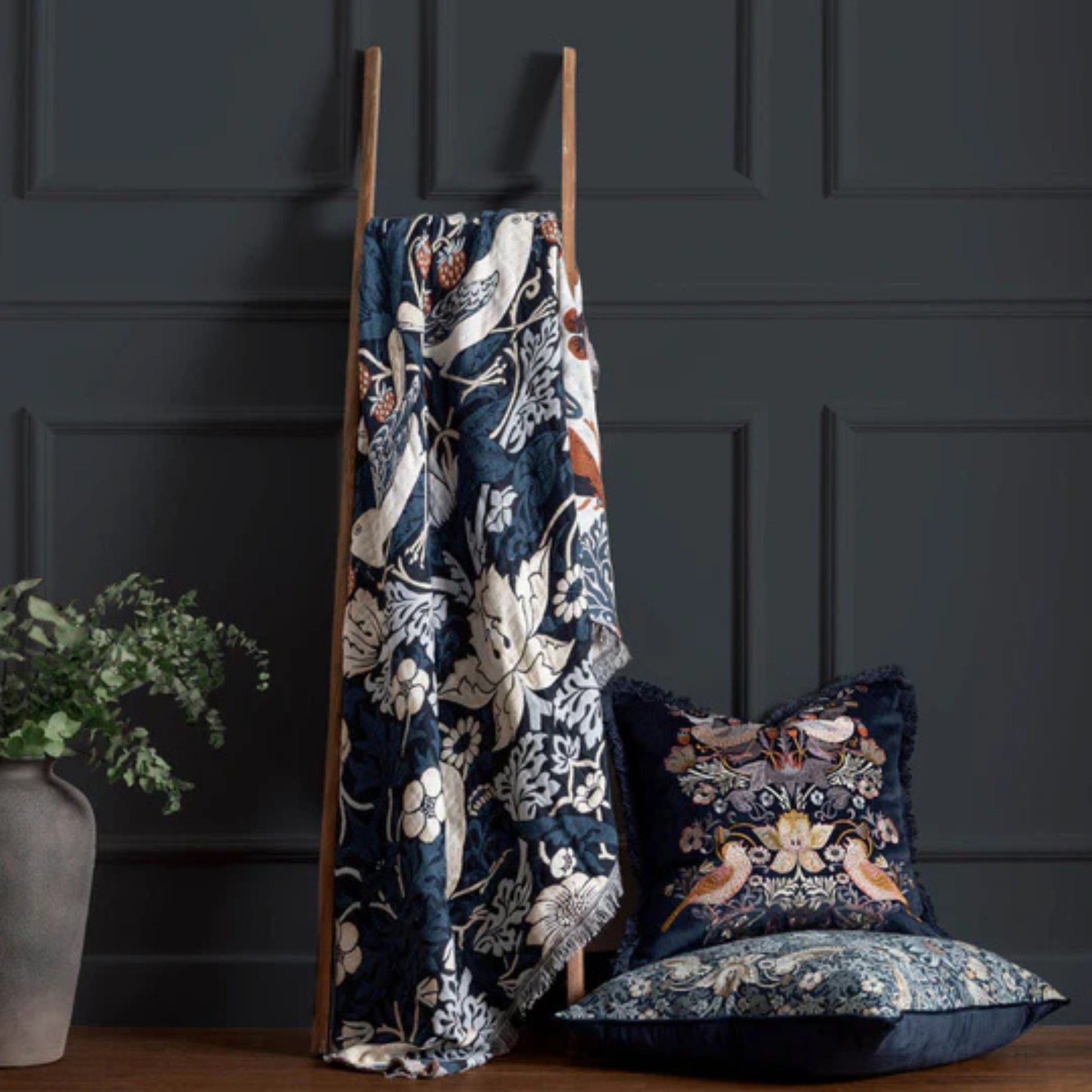Floral-patterned blanket and pillows on a wooden ladder against a dark paneled wall.