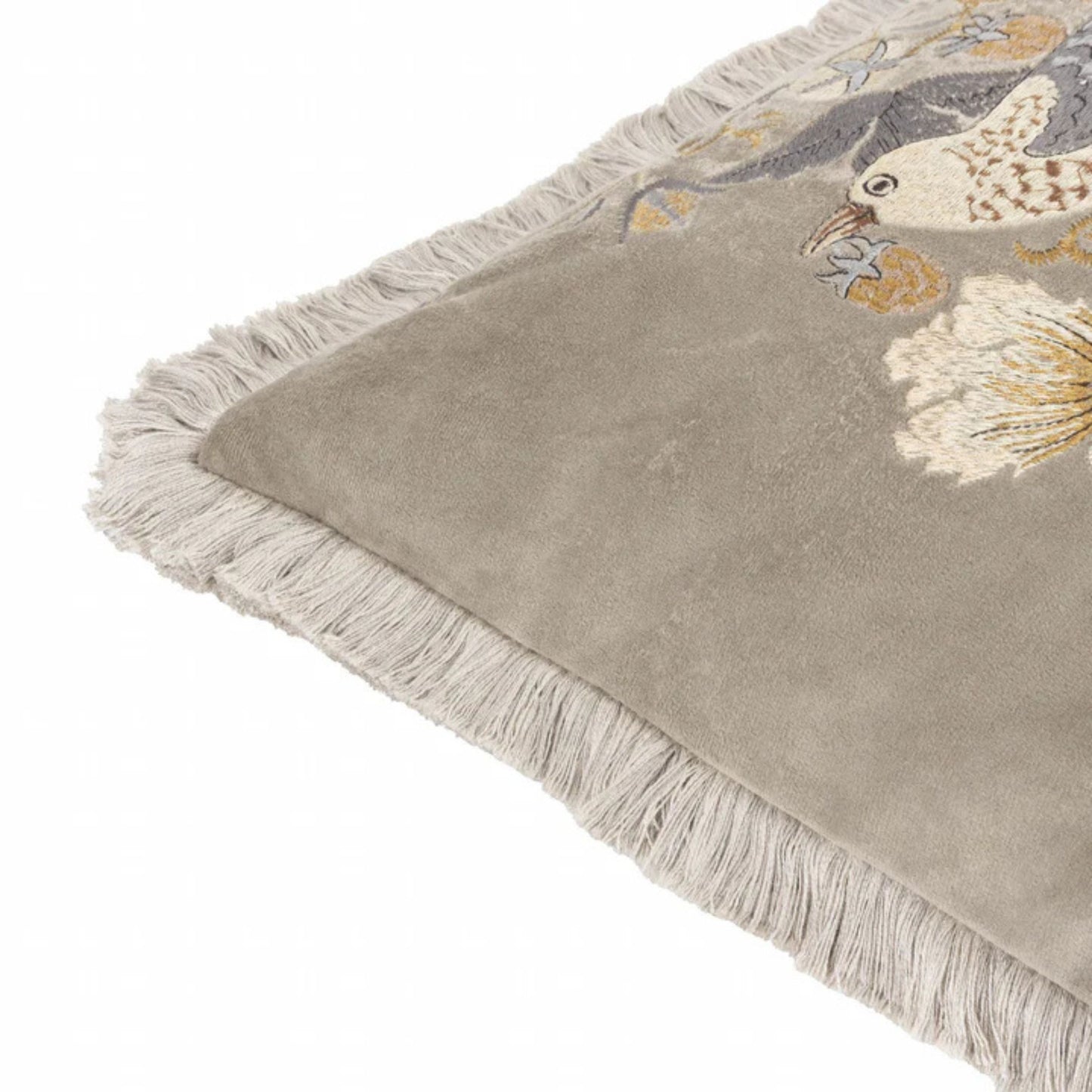 Corner detail of A square-shaped, biscuit coloured velvet cushion with a floral and animal embroidery pattern, featuring birds and surrounding floral designs, finished with an accent fringed edging.