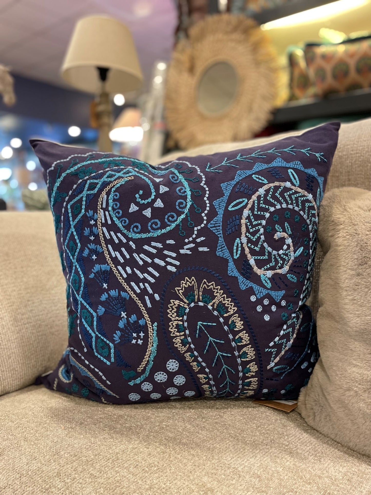 Navy cushion with blue embroidered pattern sitting in the corner of beige sofa