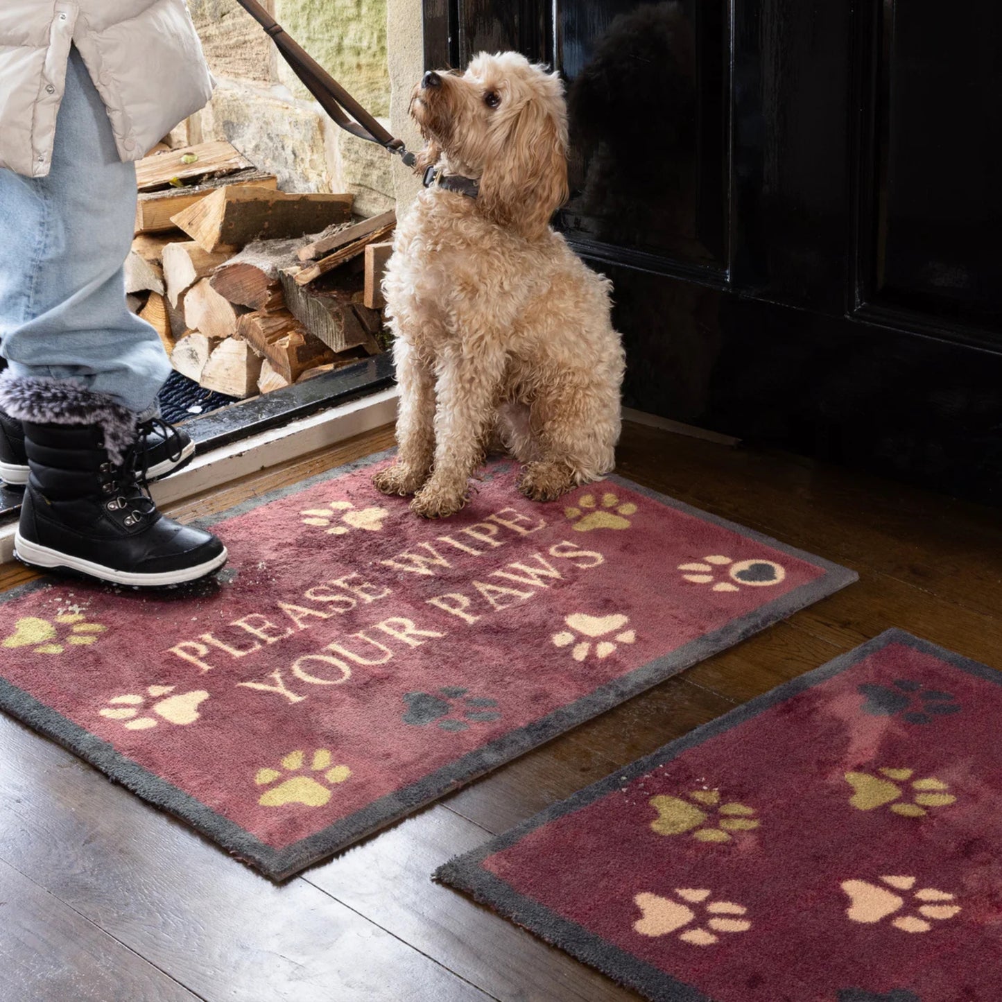 Burgandy mats with paw print design in an entrance way with a black open front door and a person with a dog on alead