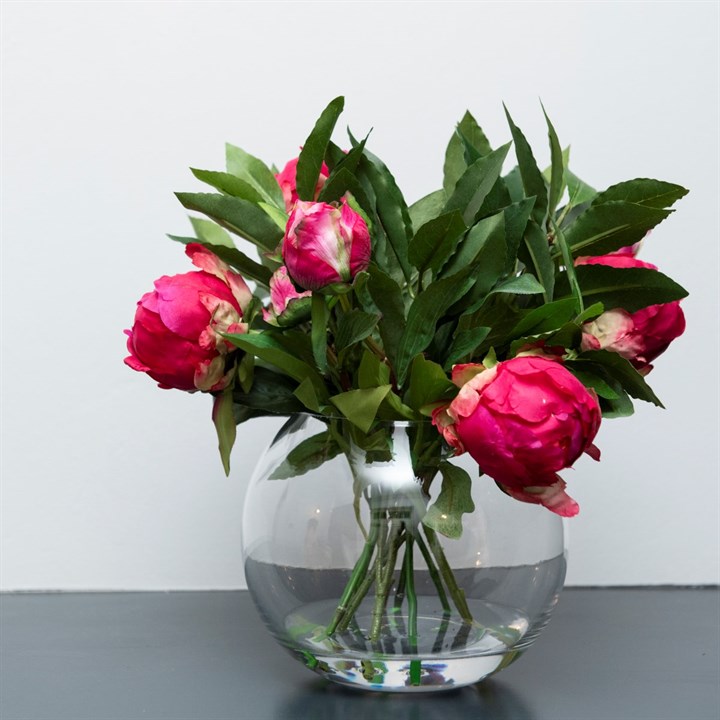 A bouquet of dark pink peonies arranged in a clear glass globe vase.
