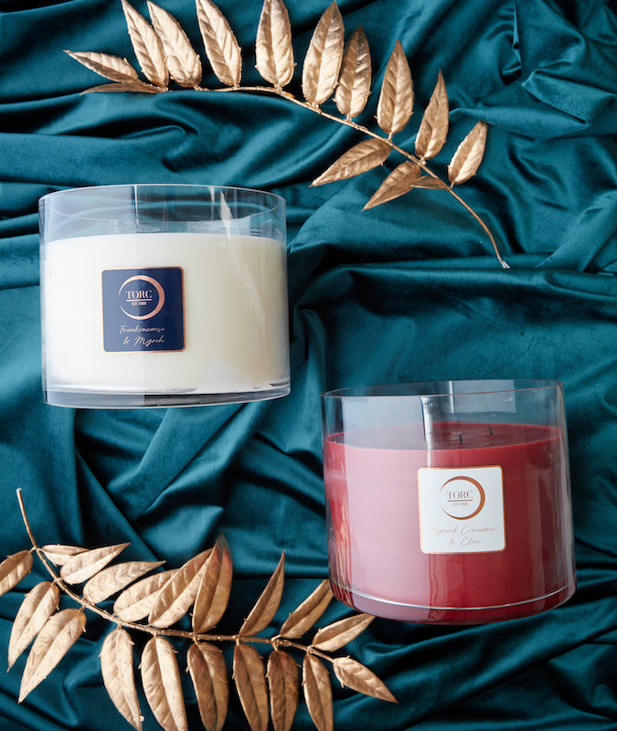 a red and a white large candle in glass containers on a silk teal fabric background with gold decorative leaves