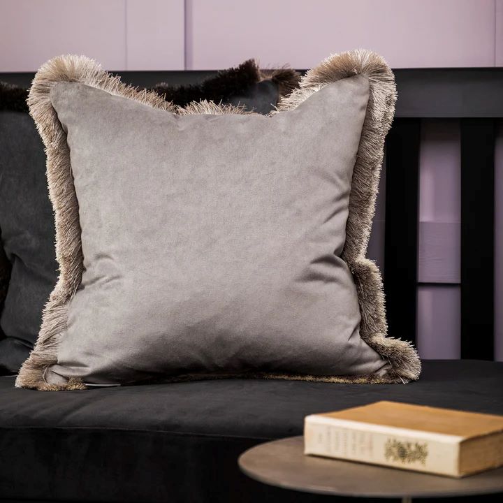 Lapis cushion in silver white with fringe trim on a dark sofa