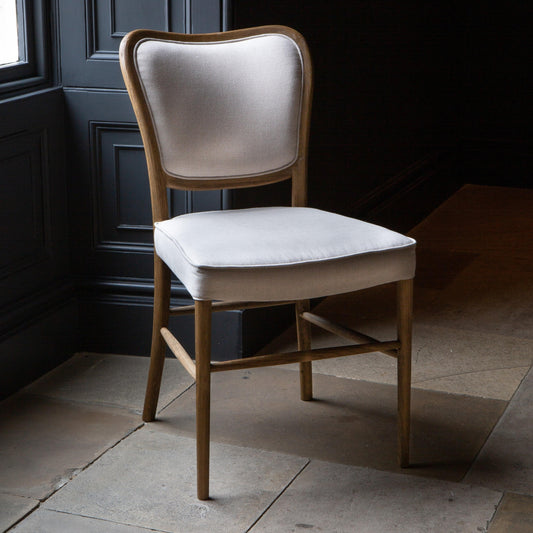 Cream upholstered back dining chair and linen seat pad on a dark moody background