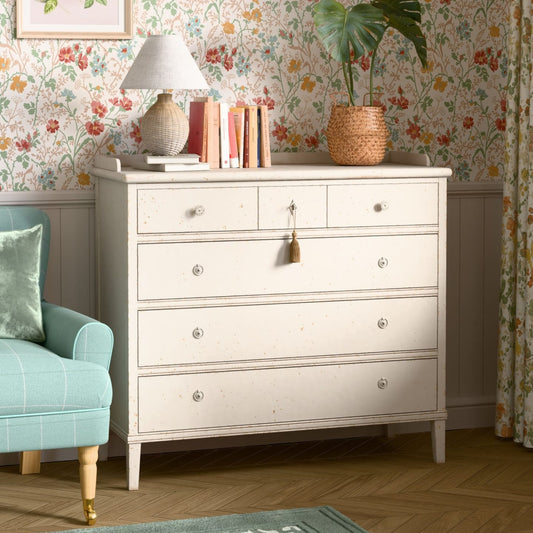 White dresser with decorative items against a floral wallpapered wall.