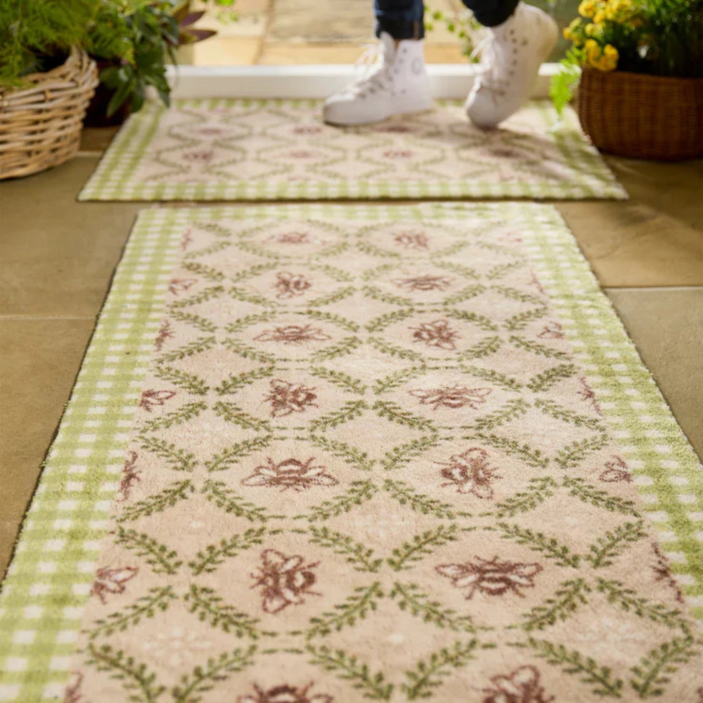 Decorative rug with floral pattern on a wooden floor, with feet wearing white sneakers in the background.