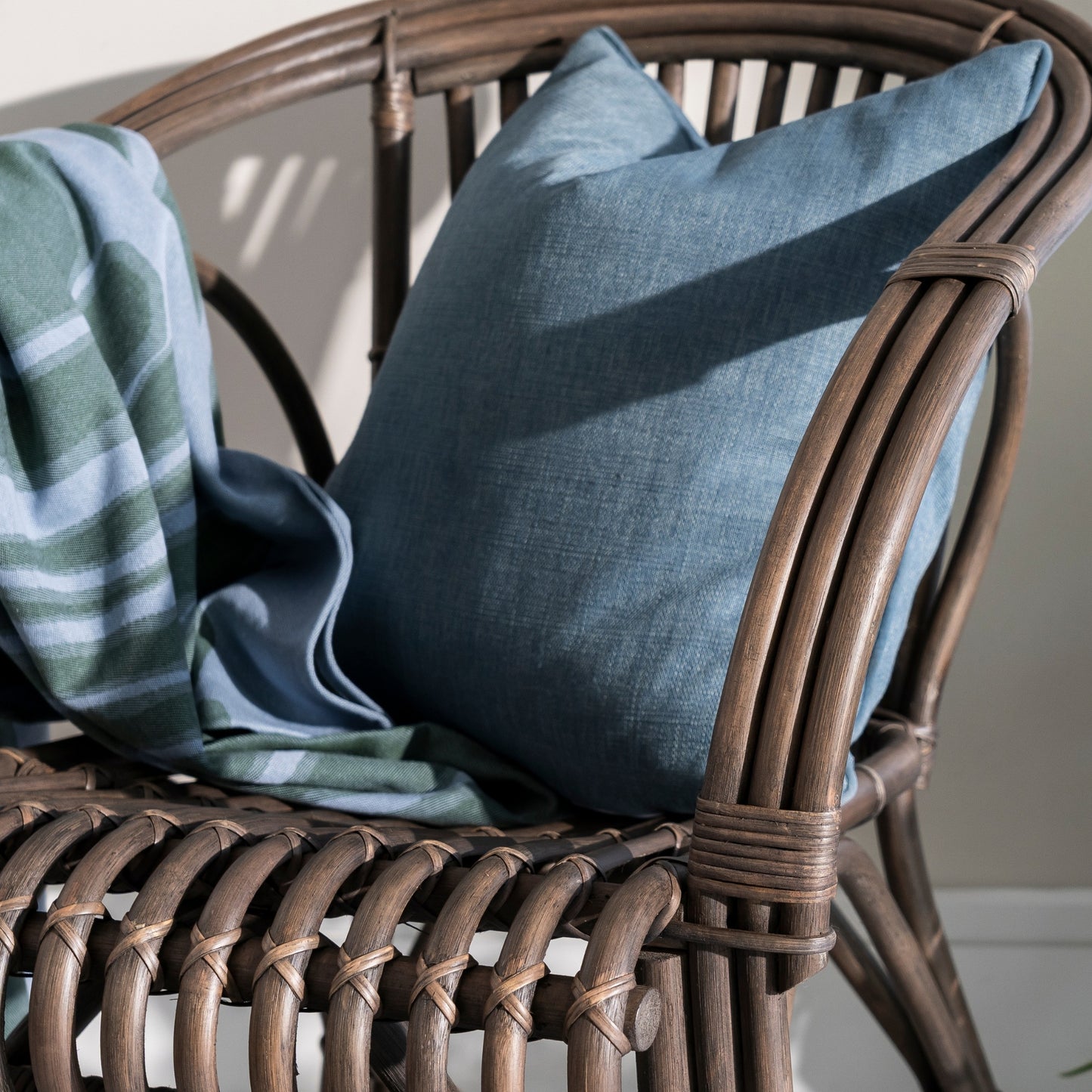 Wicker chair with a blue pillow and green blanket on a neutral background