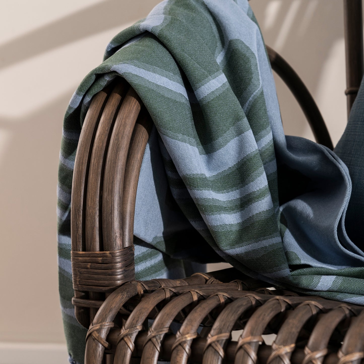 Wicker chair with a green and blue striped blanket draped over it