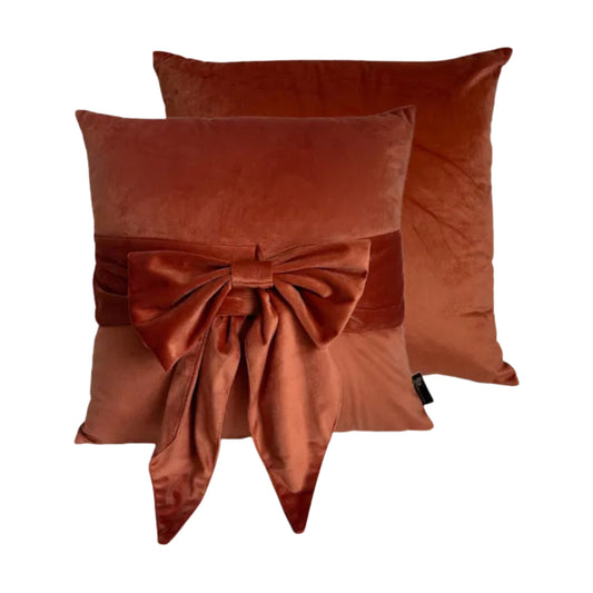 Two rust-colored pillows with a large bow on a white background