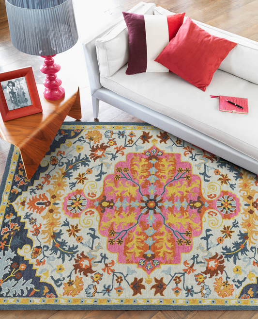 A multicolored wool rug with a distinctive Persian medallion design, placed on a floor in a room with a white sofa, showcasing its vibrant colors.