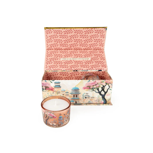 Decorative candle in a matching box with floral and architectural design on a white background