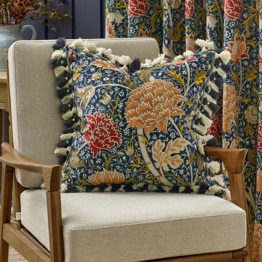 Vibrant floral tasseled cushion on a beige armchair in a room setting with floral curtains in the background