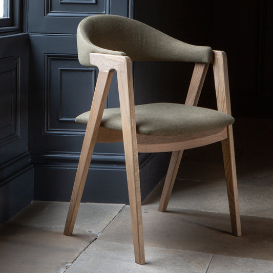 Green fabric dining chair with wood arm and legs on a stone floor with dark wood wall background