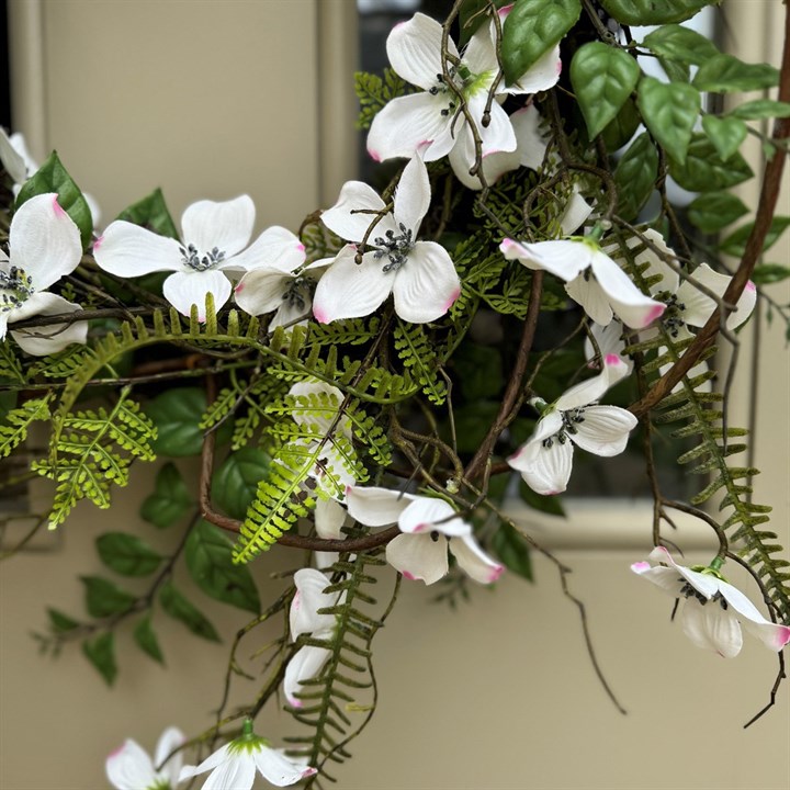 Detail of A faux Dogwood & Fern wreath with green leaves and white flowers, hanging on a light green door 
