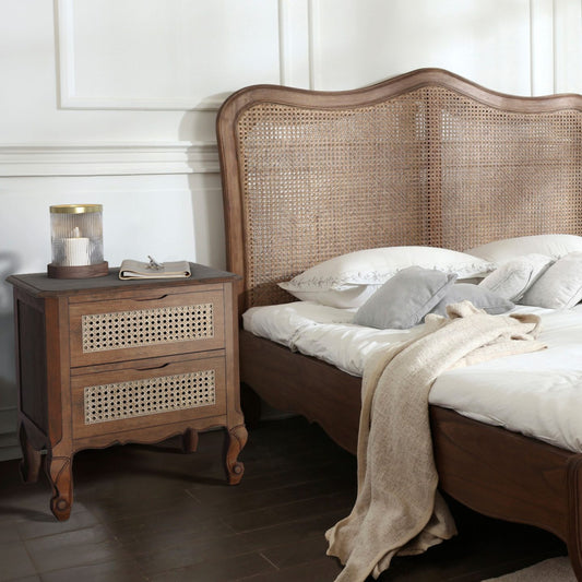 A walnut 2-drawer bedside chest with brass fittings, placed beside a bed with a beige bedding set.