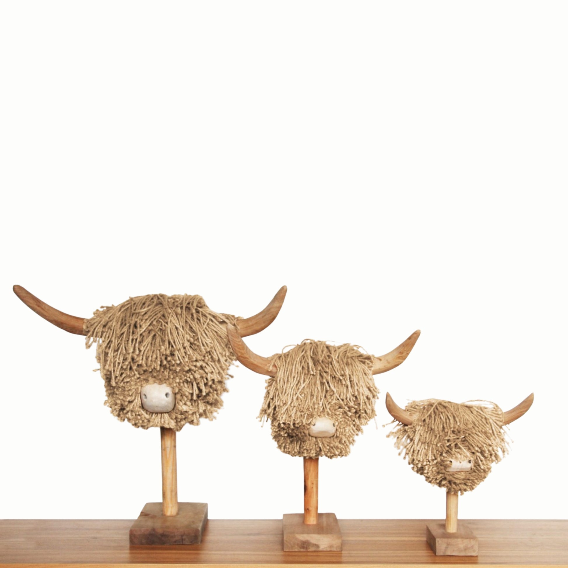 Three decorative heads of highland cows made from jute on wooden stands against a white background.