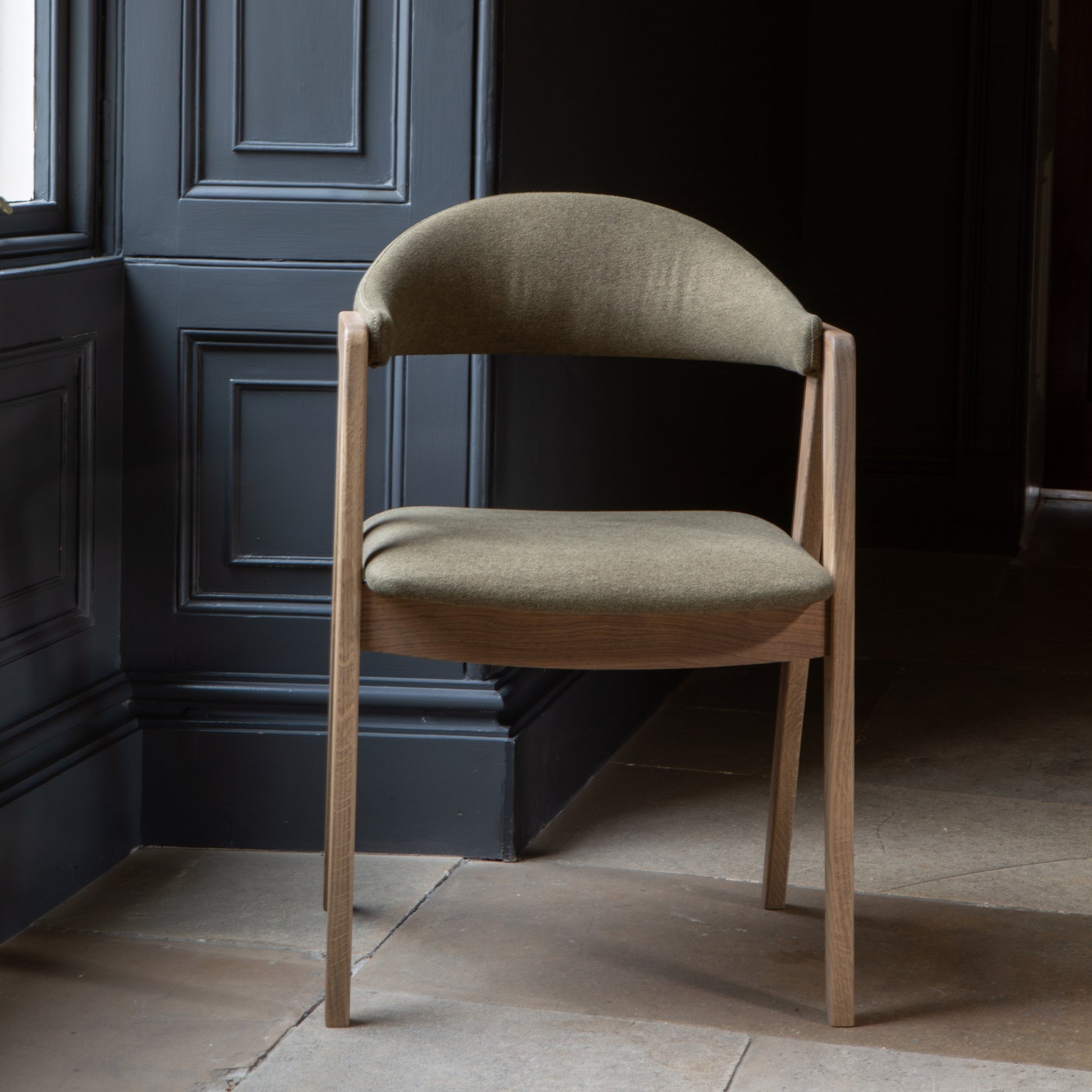 Curved back green fabric dining chair with wood arms and legs on a adark background 
