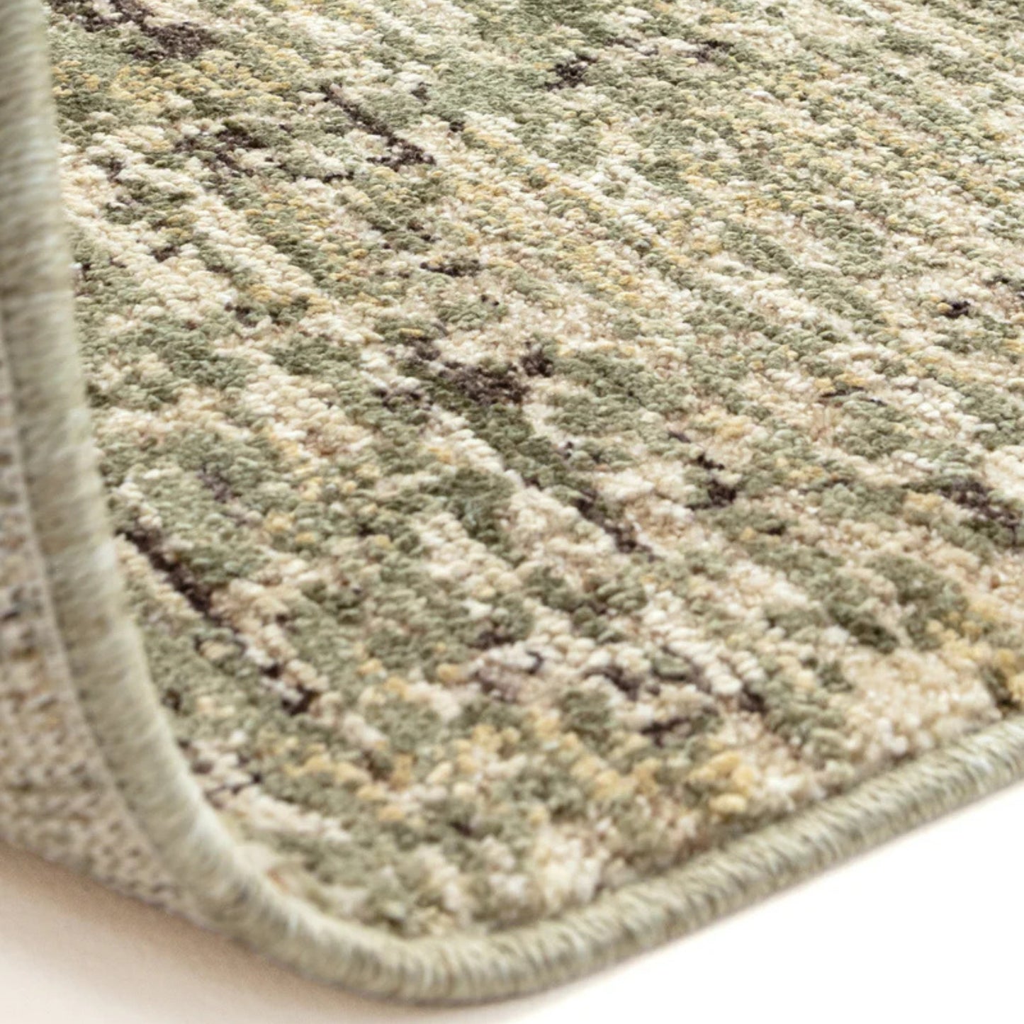 Close-up of a textured green and beige rug corner on a white background