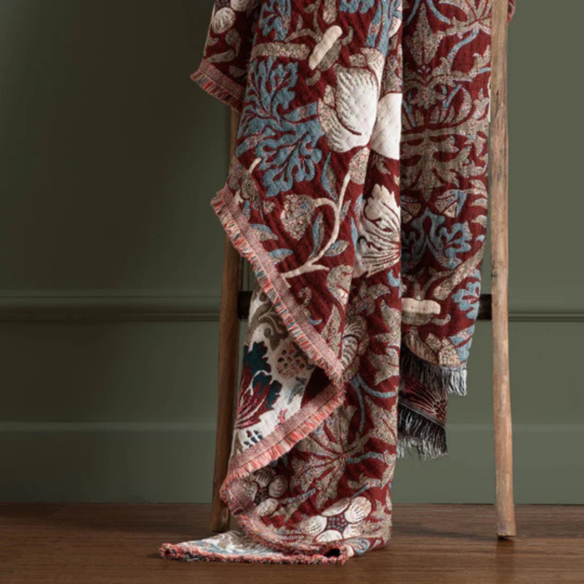 Decorative blanket with intricate patterns draped over a wooden chair against a green wall.